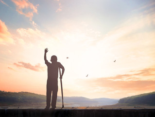 Wall Mural - Heal and rehabilitation concept: Silhouette a disabled man standing up and  at meadow sunset background