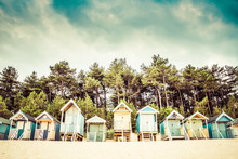 A Row Of Beach Huts On The Sandy Beach Of Wells Next The Sea In Norfolk, UK With A Tree Line And Summer Sky.