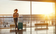 © JenkoAtaman - young woman waiting for flying at airport at window with suitcase  .