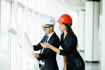 The two engineers stand near the panoramic window and gesture on construction plan