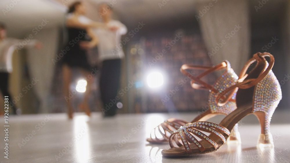 Blurred professional man and woman dancing Latin dance in costumes in the Studio, ballroom shoes in the foreground - obrazy, fototapety, plakaty 