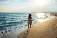 Young Woman Walk On An Empty Wild Beach Towards Celestial Beams Of Light Falling From The Sky, The Concept Of Travel And Tourism, Leisure At Sea