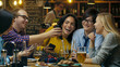 © Gorodenkoff - In the Bar/ Restaurant Birthday Party Celebration in Progress Beautiful Young People Show Their Mobile Phone Screens and Have Great Fun.
