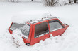 Red car under snow in snowbank after blizzard