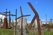 Stary cmentarz katolicki z pordzewiałymi, pokrzywionymi krzyżami, niektóre bez jednego ramienia, w tle kamienne stare nagrobki, błękitne niebo, słonecznie