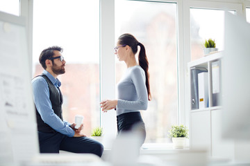 Wall Mural - Two colleagues with drinks having talk by office window while having break