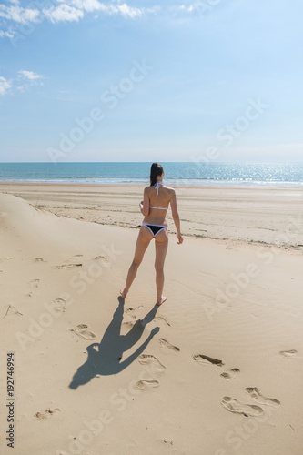 Fotografía Unrecognizable woman in bikini walks down the beach along the seashore leave footprints on the sand