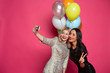 © My Ocean studio - Two cheerful and beautiful smiling girlfriend photographed themselves on the phone or make a selfie on a pink background.