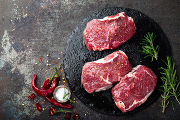 Raw beef meat. Fresh steaks on slate board on black background. Top view