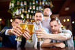 © Seventyfour - Group of cheerful friends clinking beer glasses together while sitting at bar counter and  celebrating end of work week, focus on foreground