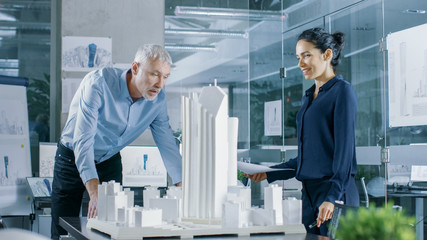 Aufkleber - In the Architectural Bureau Female Engineer Brings Blueprints and Shows them to  Senior Architect, They Discuss Project. They Work as Urban Planners on a Building Model.