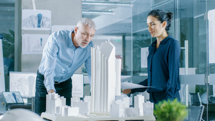 Aufkleber - In the Architectural Bureau Female Engineer Brings Blueprints and Shows them to  Senior Architect, They Discuss Project. They Work as Urban Planners on a Building Model.