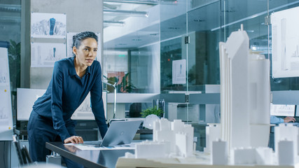 Aufkleber - Female Architectural Designer Works on a Laptop,  Engineering New Building Model for the Urban Planning Project. Clean Minimalistic Office, Concrete Walls Covered by Blueprints and Documents.