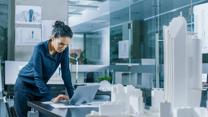 Aufkleber - Female Architectural Designer Works on a Laptop,  Engineering New Building Model for the Urban Planning Project. Clean Minimalistic Office, Concrete Walls Covered by Blueprints and Documents.