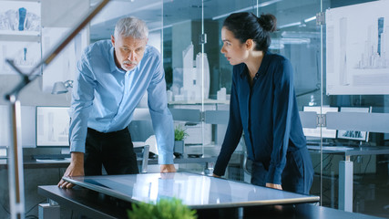 Wall Mural - Senior Male and Young Female Architectural Designers Draw Building Concept on a Graphics Tablet Display Vertical Touchscreen Table. They Use Gestures for Zooming Project Model.