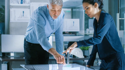 Canvas Print - Senior Male and Young Female Architectural Designers Draw Building Concept on a GraphicsTablet Display Vertical Touchscreen Table. They Use Gestures for Zooming Project Model.