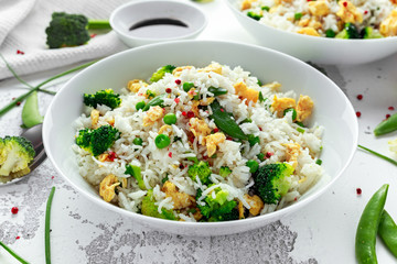 Fried rice with vegetables, broccoli, peas and eggs in a white bowl. soy sauce. healthy food