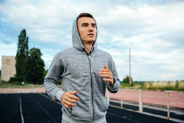 Close-up portrait of a handsome running sportsman, wearing sweatshirt with hood and listening to music, at the stadium