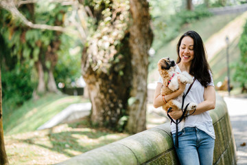 Portrait of a young, attractive Asian pan woman in the park with her shih tzuh dog. They're in the middle of a park and look happy and relaxed.