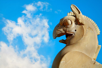 Fragment of stone column sculpture of a Griffin in Persepolis against a blue sky with clouds. Ancient Achaemenid Kingdom. Iran. Persia.