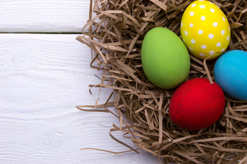 Wall Mural - Colored easter eggs in nest top view on white wooden background