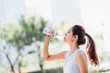 Shot of a young Asian woman drinking water from water bottle after jogging in the park.