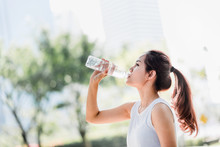 Shot Of A Young Asian Woman Drinking Water From Water Bottle After Jogging In The Park.