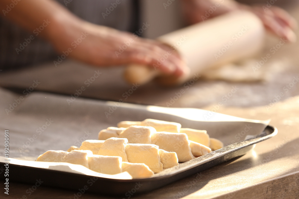 Baking sheet with raw croissants and blurred woman on background