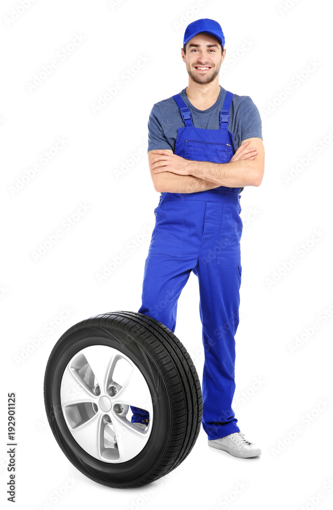 Young mechanic in uniform with car tire on white background