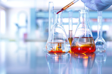 glass flask with hand of scientist drop orange solution in blue chemistry science research laborator