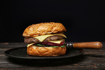 Wall Mural - Tasty burger on plate against dark background