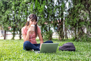 Asian girl on the grass using laptop and hearing music