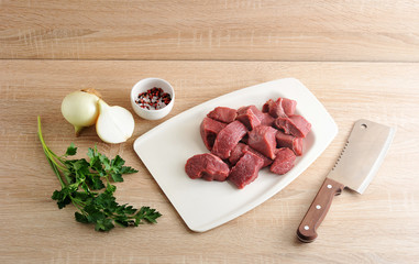 Wall Mural - A set for cooking minced meat. Pieces of beef on a white tray, onion, parsley and a cup of pepper and salt. Next a knife for cutting meat. Light wooden background.