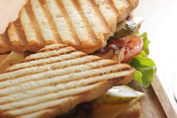 Two sandwiches from roasted bread on a wooden tray. As a filling for sandwiches used chicken breast, bacon, green salad, cheese, tomatoes and pickles. View from above. Close-up. Macro photography.