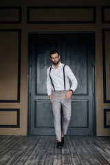 handsome elegant man posing in white shirt and suspenders against door