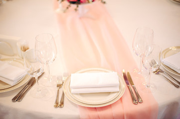 Elegant plate with napkin, cutlery and wine glasses on the peach color tablecloth