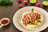 Fototapeta Dziecięca - Grilled chicken fillet is cut into slices on a cushion of mashed potatoes with vegetables - onion, garlic, pepper, cabbage, radish, greens in a large beige dish on a dark wooden table.