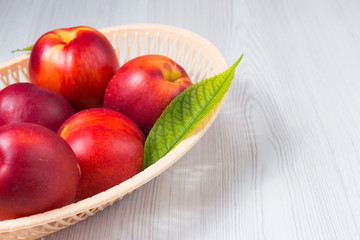 Wall Mural - Peaches in a basket with leaves on a white wooden table with space for text