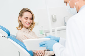 Doctor and smiling patient looking at tablet screen in modern dental clinic