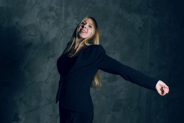 Attractive pretty young model posing against a dark studio background with copy space looking. Atomic blonde woman stands with widely spread arms. Fashion style