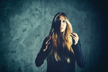 Attractive pretty young model posing against a dark studio background with copy space looking. Atomic blonde woman straightens her magnificent hair. Dramatic look