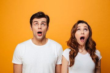 Poster - Photo of excited boyfriend and girlfriend in white t-shirts looking on camera with open mouth, isolated over yellow background