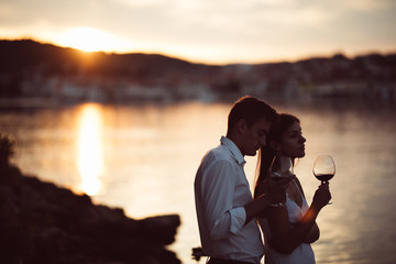 Two young people enjoying a glass of red wine in the sunset on the seaside.Healthy glass od homemade red wine,Mediterranean culture.Warm climates,seaside living couple.Seaside vacation experience