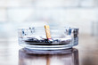 Cigarette butts and ashes in a glass ashtray.