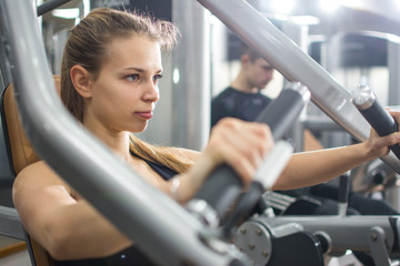 Wall Mural - Close up portrait of sporty blonde girl workout on exercise machine in gym.