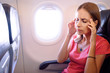 Fear of flying woman in plane airsick with stress headache and motion sickness or airsickness. Person in airplane with aerophobia scared of flying being afraid while sitting in airplane seat.