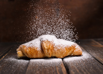 Wall Mural - croissant on wooden desk with falling powdered sugar