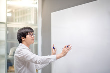 Young Asian Man Writing On White Board In Conference Room. Business Meeting Presentation Concept