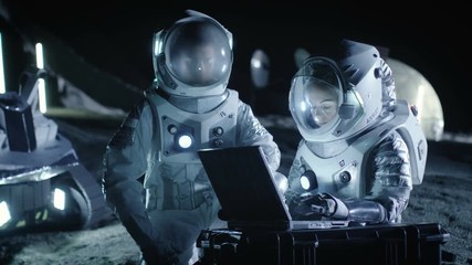 Wall Mural - two astronauts wearing space suits work on a laptop, exploring newly discovered planet, send communi