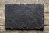 Fototapeta Desenie - Black slate board on grunge wooden table closeup. Natural texture. Can be used like food background